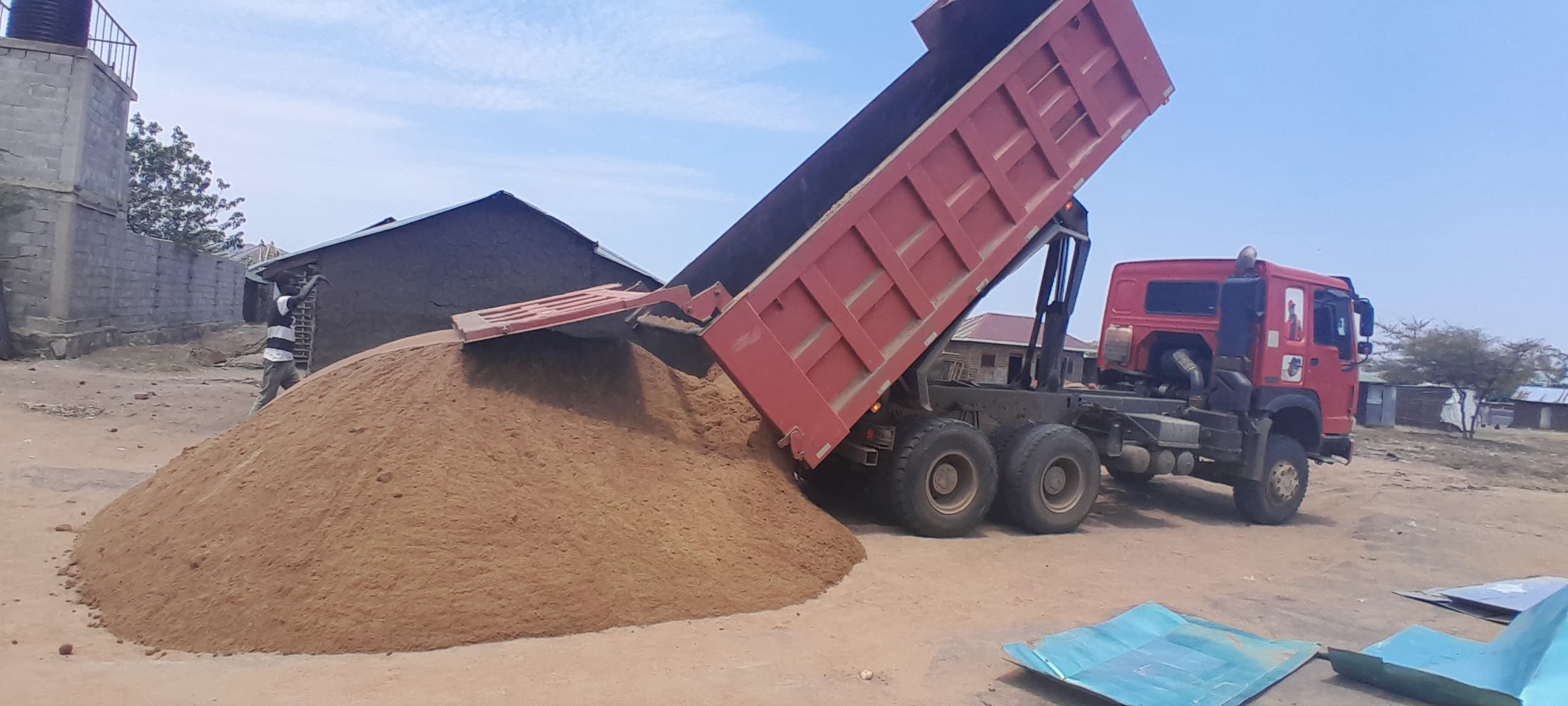 A red pickup truck offloading sand in Juba, South Sudan