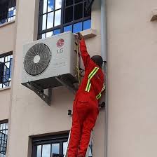 A technician installing an AC fan outside high up on wall in Juba, South Sudan